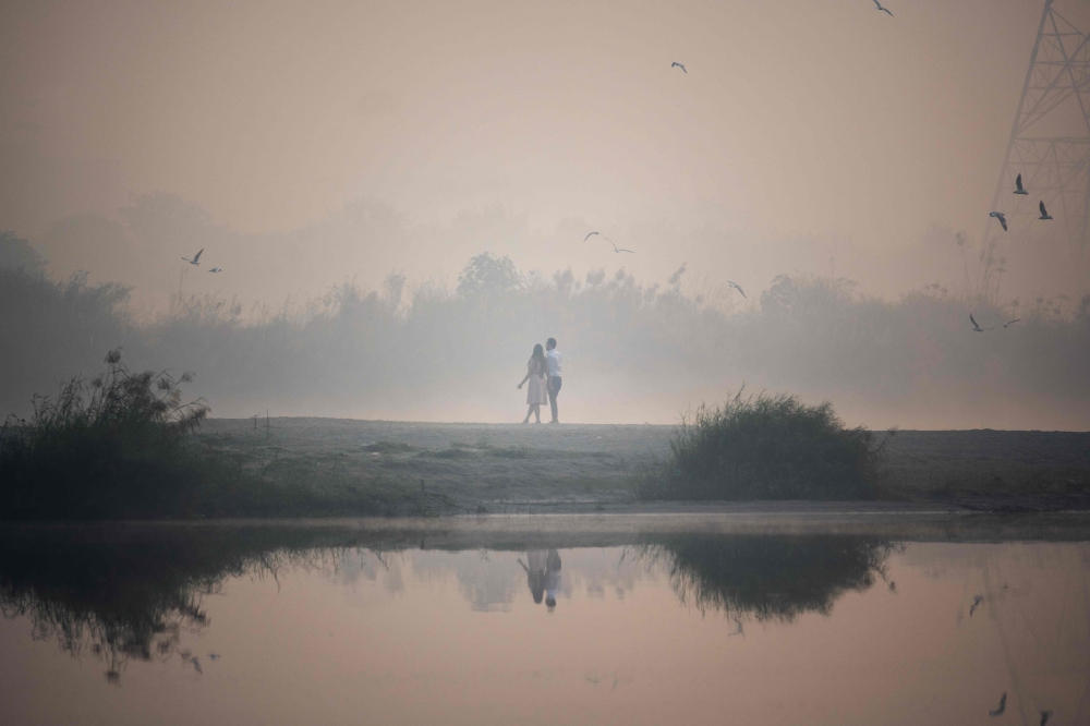 A couple has their pictures taken on the banks of the Yamuna River during a smoggy morning at sunrise in New Delhi on October 29, 2020. AFP / Jewel Samad 