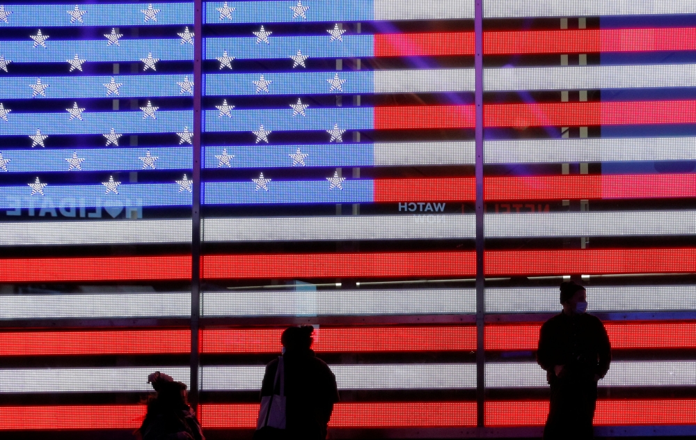 People stand next to a screen displaying a U.S. flag in Times Square during the 2020 U.S. presidential election in New York City, New York, U.S. November 4, 2020. REUTERS/Brendan McDermid