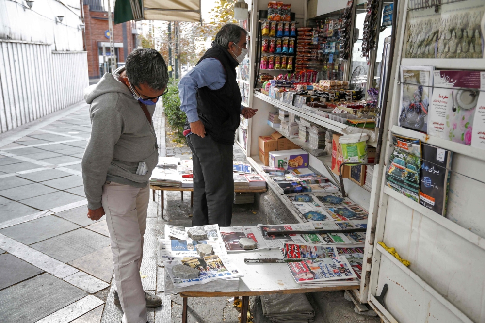 A man browses the headlines of Iranian Farsi newspapers featuring the 2020 US general election results at a news stand in Iran's capital Tehran on November 8, 2020. / AFP / ATTA KENARE