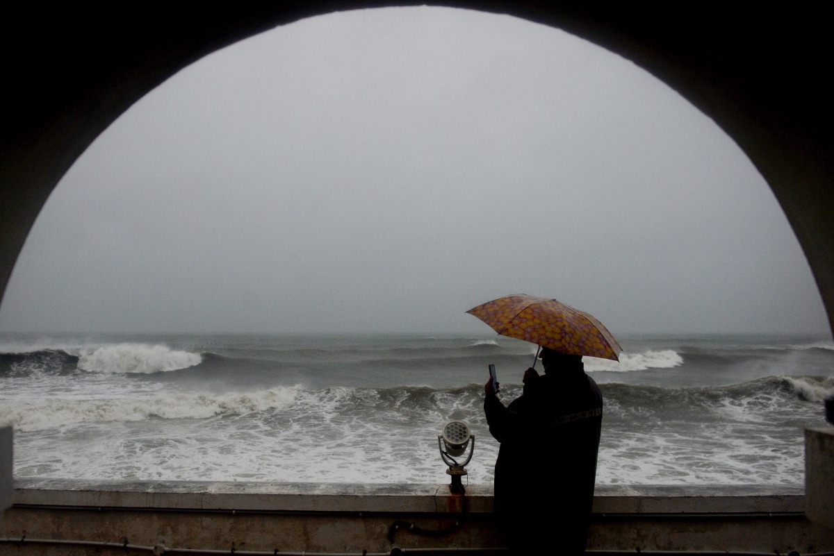 A man shelters under an umbrella from heavy rains while looking out to the Indian ocean as Cyclone Nivar approaches the southeastern Indian coast in Puducherry on November 25, 2020. Several thousand people in south-eastern India fled their homes on Novemb