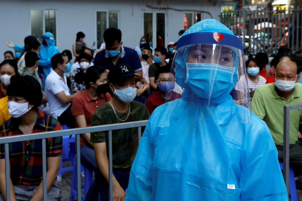 A healthcare worker wearing protective suit walks past as local residents, who have returned after travelling to Da Nang, wait at a coronavirus disease (COVID-19) testing center in Hanoi, Vietnam August 10, 2020. REUTERS/Kham/File Photo