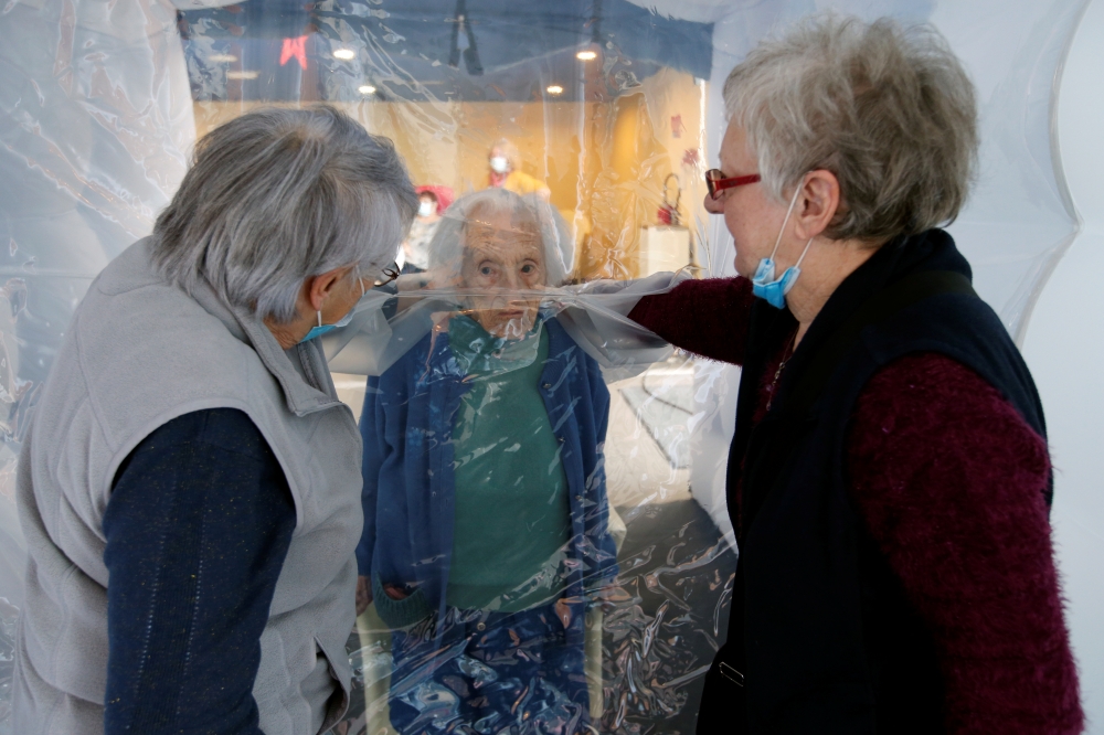 Marie-Paule and Marie-Josephe interact with their mother Colette, 97 old, behind a removable plastic sheet inside a bubble structure which allows families to give hugs without risk of contamination or transmission of Covid-19. Reuters/Pascal Rossignol