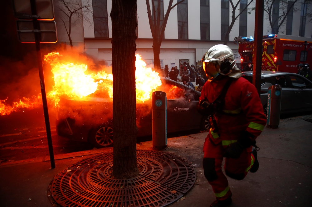 A firefighter runs past a burning car during a protest against the 
