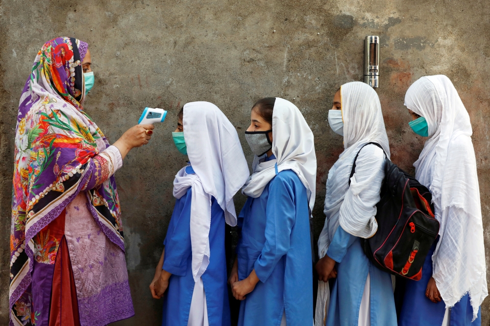 Students wear protective face masks as they have their temperature checked before entering a class, after the government allowed the reopening of schools from grade six to eight amid the coronavirus disease (COVID-19) pandemic, in Peshawar, Pakistan Septe