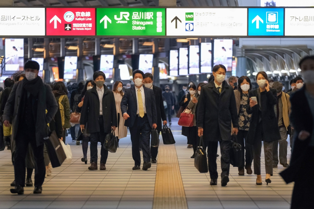 Commuters wearing face masks walk along a concourse at Shinagawa station in Tokyo on December 10, 2020. / AFP / Kazuhiro NOGI