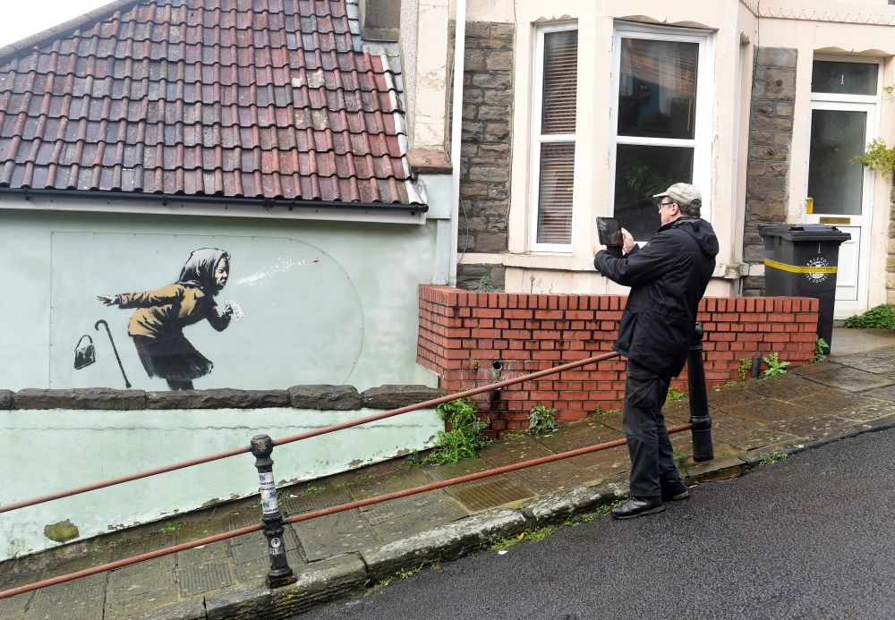 A man takes pictures of a new street artwork entitled 'Aachoo!!' by Banksy in Totterdown, Bristol, Britain December 11, 2020. REUTERS/Rebecca Naden