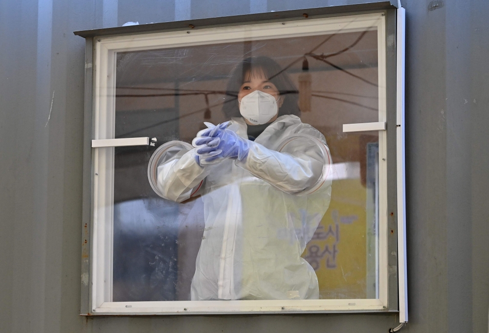 A medical staff member wearing protective gear waits in a booth for visitors to take samples for the Covid-19 coronavirus test at a temporary testing station outside a railway station in Seoul on December 16, 2020 as South Korea ramps up coronavirus check