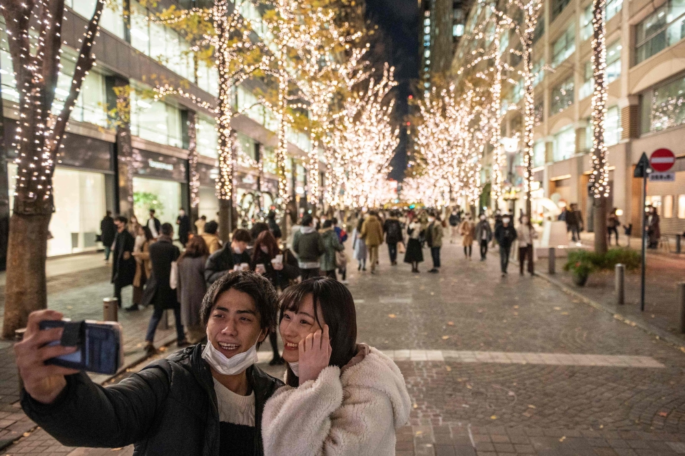 A couple takes pictures in front of Christmas-themed light decorations along a street in Marunouchi district in Tokyo on December 25, 2020. / AFP / Philip FONG