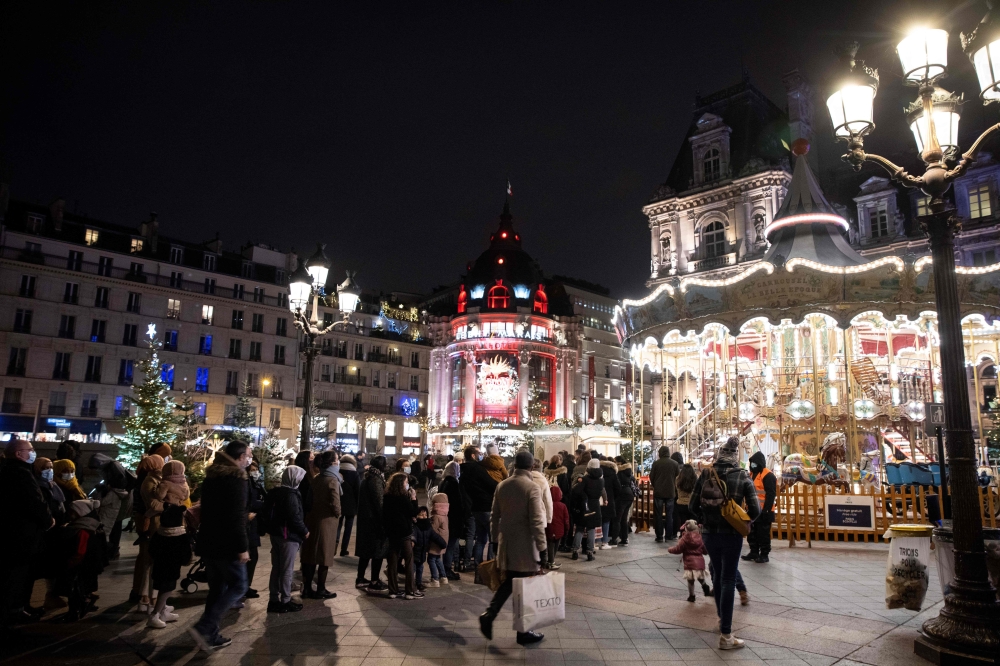 People gather near a merry-go-round on the Place de l'Hotel de Ville in Paris, where the city has set up a christmas village, on December 26, 2020. / AFP / Thomas SAMSON