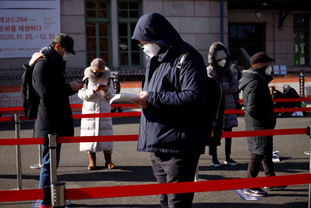 A man reads a book while waiting in a line to undergo coronavirus disease (COVID-19) test at a coronavirus testing site which is temporarily set up in front of a railway station on Christmas day in Seoul, South Korea, December 25, 2020. REUTERS/Kim Hong-J
