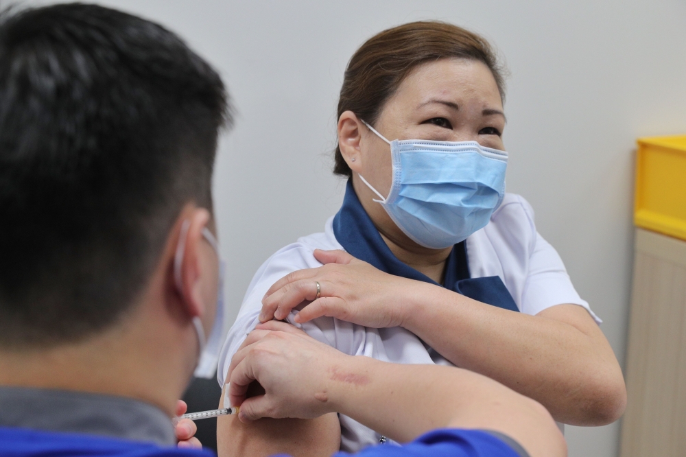 This handout photo taken and released on December 30, 2020 by Singapore's Ministry of Communications and Information shows the COVID-19 coronavirus vaccine being given to senior staff nurse Sarah Lim (R) as Singapore began its vaccination exercise with th