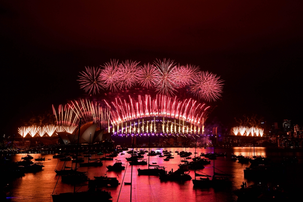 New Year's Eve fireworks erupt over Sydney's iconic Harbour Bridge and Opera House (L) during the fireworks show on January 1, 2021. / AFP / SAEED KHAN