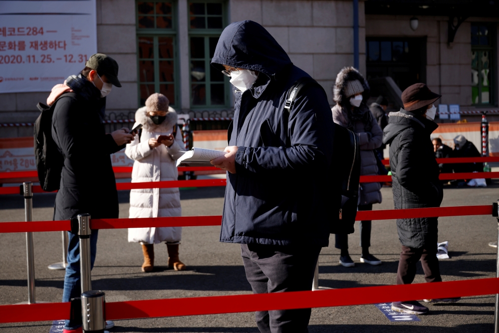 A man reads a book while waiting in a line to undergo coronavirus disease (COVID-19) test at a coronavirus testing site which is temporarily set up in front of a railway station on Christmas day in Seoul, South Korea, December 25, 2020. REUTERS/Kim Hong-J