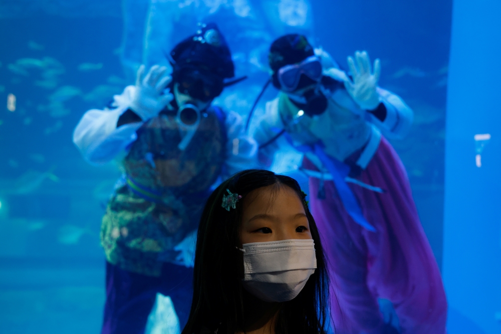 A girl wearing a mask poses for photographs in front of divers in Korean traditional costumes 