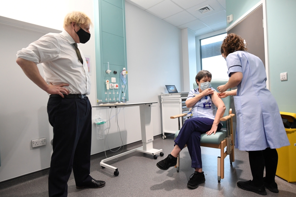Britain's Prime Minister Boris Johnson looks on as junior sister Susan Cole receives the Oxford University/AstraZeneca COVID-19 vaccine during his visit at the Chase Farm Hospital, in north London, Britain January 4, 2021. Stefan Rousseau/Pool via Reuters
