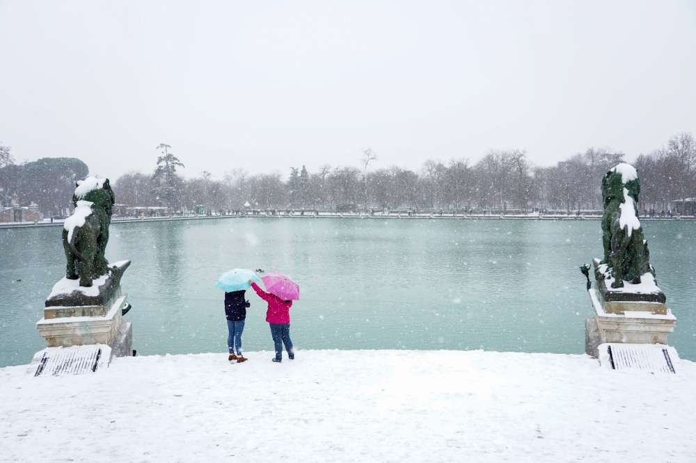 People carry umbrellas during heavy snowfall in Retiro park in Madrid, Spain, January 8, 2021. REUTERS/Juan Medina