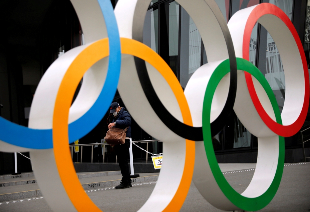 A man wearing a protective mask against COVID-19 is seen through the Olympic rings in Tokyo, Japan January 8, 2021. REUTERS/Issei Kato/File Photo