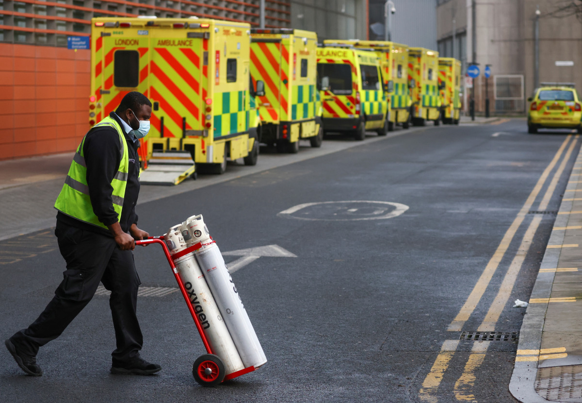 A worker pushes a trolley with the oxygen cylinders as ambulances queue at the Royal London Hospital amidst the spread of the coronavirus disease (COVID-19) pandemic, in London, Britain, January 9, 2021. REUTERS/Simon Dawson
