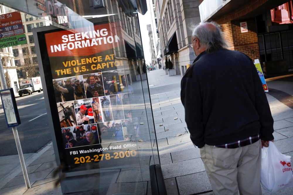 A local resident looks at a billboard with pictures of supporters of US President Donald Trump wanted by the FBI who participated in storming the U.S. Capitol in Washington, U.S., January 13, 2021. Reuters/Carlos Barria