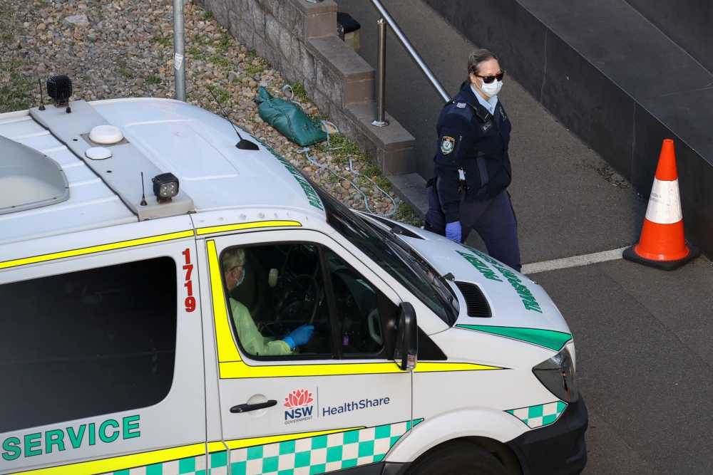 A police officer watches an entrance to a quarantine hotel, where returning travelers are kept in isolation for a period to curb the spread of the coronavirus disease (COVID-19), as a patient transport service vehicle departs in Sydney, Australia, August 