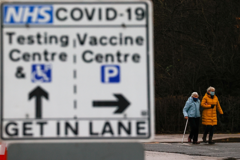 People walk behind a sign showing the way to the NHS Vaccination Centre and the testing centre parking lots, amid the coronavirus disease (COVID-19) outbreak, in Manchester, Britain January 11, 2021. REUTERS/Phil Noble/File Photo