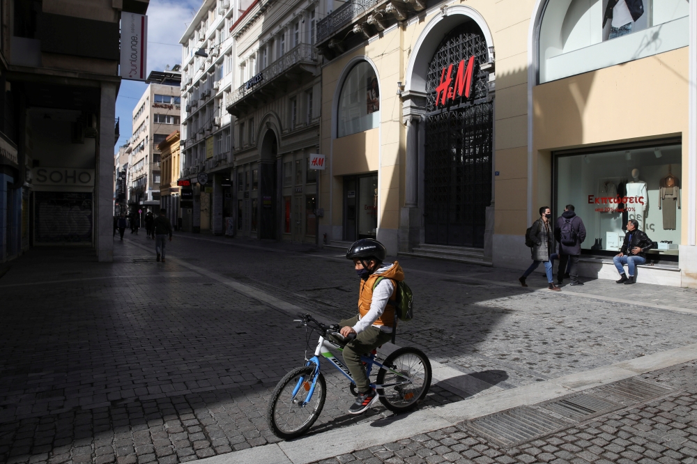 A child rides a bike past a closed shop, amid lockdown restrictions due to the spread of the coronavirus disease (COVID-19) pandemic, in Athens, Greece, February 6, 2021. REUTERS/Costas Baltas