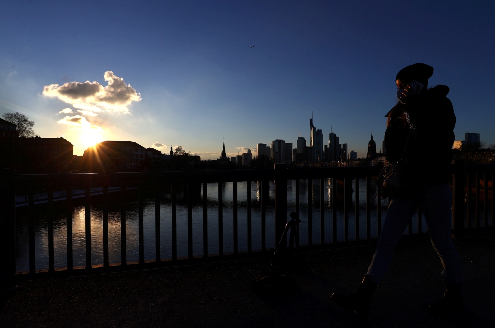 A woman wears a protective mask as she crosses a bridge in front of the skyline as the spread of the coronavirus disease (COVID-19) continues during an extended lockdown and a demand by the German government for more home office possibilities in Frankfurt
