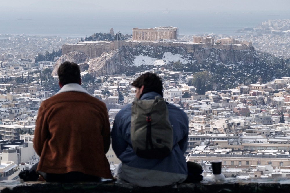 Two men sit on Lycabettus hill as the Parthenon temple is seen atop the Acropolis hill following snowfall in Athens, Greece, February 17, 2021. REUTERS/Vassilis Triandafyllou