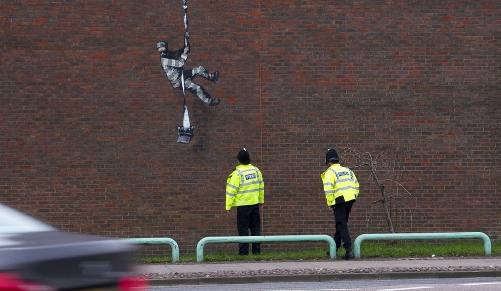 Police officers look at the mural of artist Banksy on a wall at HM Reading Prison in Reading, Britain in this picture obtained from the artist's official Instagram account. @banksy/banksy.co.uk via REUTERS