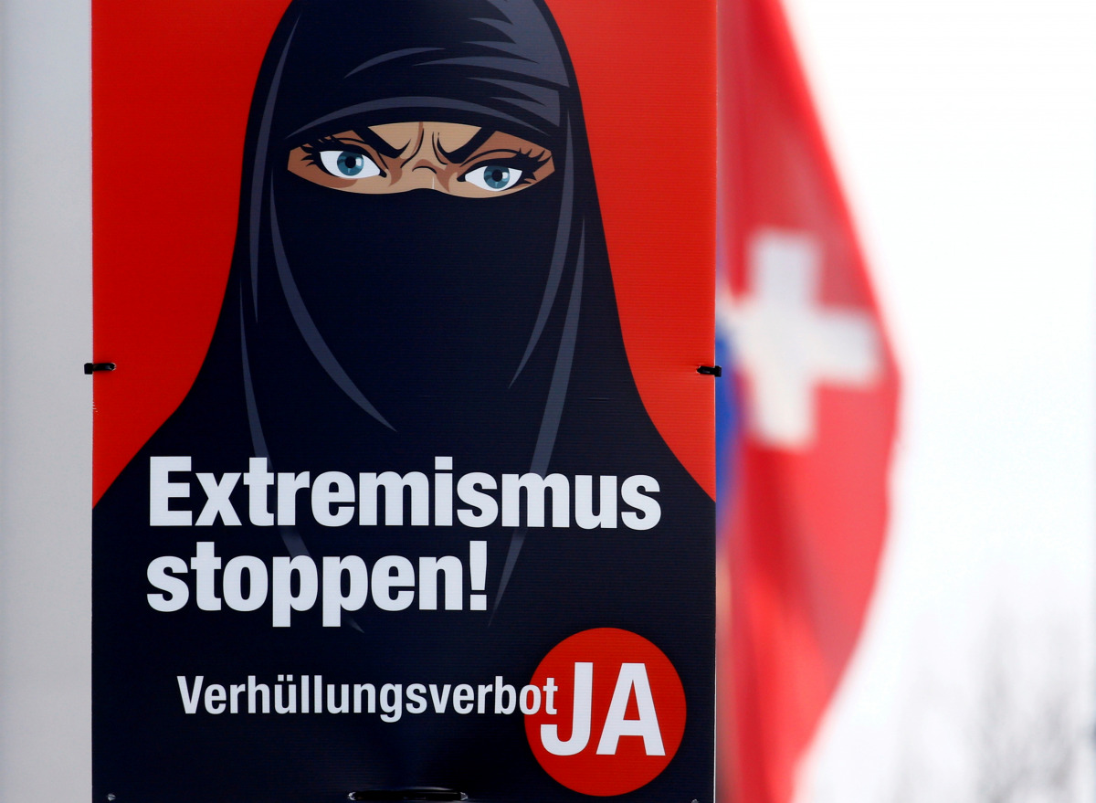 FILE PHOTO: A Swiss national flag flies behind a poster of the initiative committee against wearing the burqa (Verhuellungsverbot) reading 
