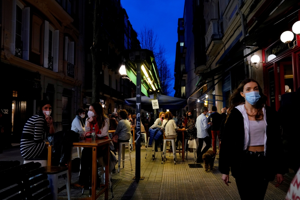 FILE PHOTO: People wearing protective masks walk past bar customers after bars reopened in Spain's Basque Country, amid the coronavirus disease (COVID-19) outbreak, in Bilbao, Spain, February 19, 2021. REUTERS/Vincent West