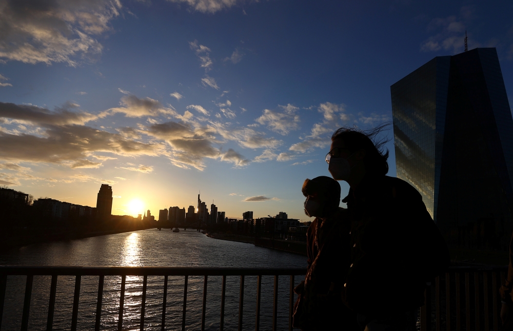 People wearing protective masks as they are crossing a bridge in front of the head quarter of the European Central Bank (ECB,R) during sunset as the spread of the coronavirus disease (COVID-19) continues in Frankfurt, Germany, March 27, 2021. REUTERS/Kai 