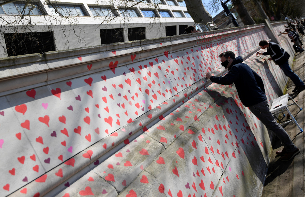 Volunteers and relatives of bereaved paint hearts along a wall beside St Thomas' hospital as a memorial to all those who have died so far in the UK from COVID-19, amid the spread of the coronavirus disease pandemic in London, Britain, March 29, 2021. REUT