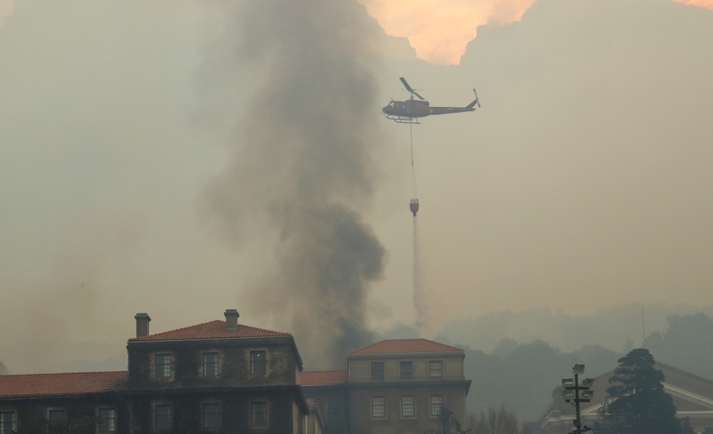 A helicopter drops water as the library at the University of Cape Town burns after a bushfire broke out on the slopes of Table Mountain in Cape Town, South Africa, April 18, 2021. REUTERS/Mike Hutchings