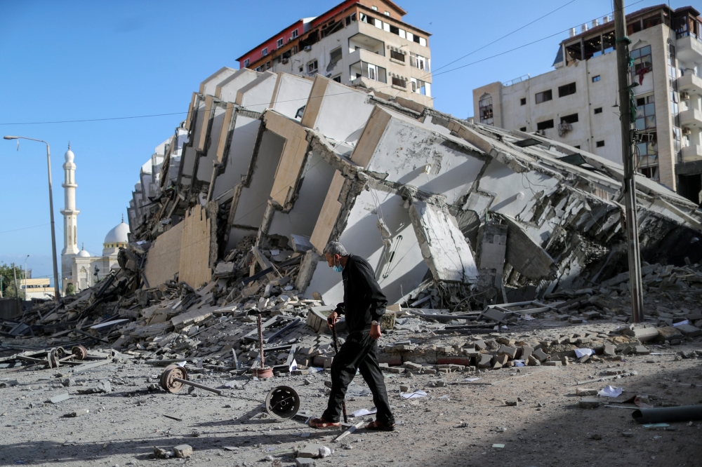 A Palestinian man walks past the remains of a tower building which was destroyed in Israeli air strikes, amid a flare-up of Israeli-Palestinian violence, in Gaza City May 12, 2021. REUTERS/Suhaib Salem