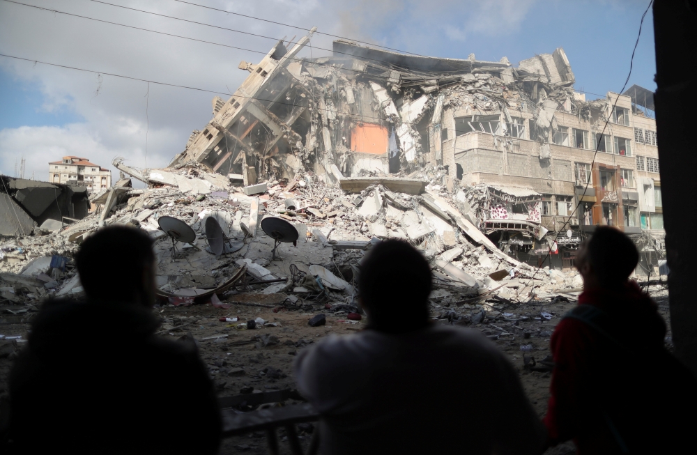 Palestinians look at the remains of a tower building which was destroyed by Israeli air strikes, amid a flare-up of Israeli-Palestinian violence, in Gaza City May 13, 2021. Reuters/Suhaib Salem