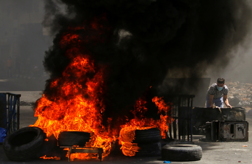 A Palestinian demonstrator sets up a barricade as tires burn during a protest over tension in Jerusalem and Israel-Gaza escalation, in Hebron in the Israeli-occupied West Bank, May 14, 2021. REUTERS/Mussa Qawasma