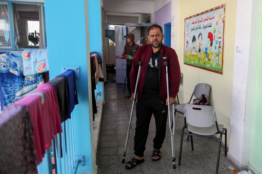 Palestinian man Ihab El-Attar, who, according to him, lost four members of his family when an Israeli strike hit their house and injured him, walks with crutches at a United Nations-run school where he takes refuge, in Gaza City May 18, 2021. REUTERS/Suha