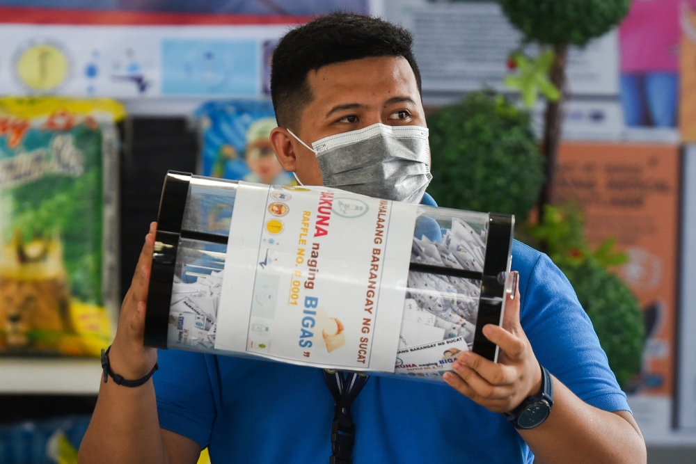 Village official Paolo Tolentino holds the raffle jar during the weekly raffle draw of sacks of rice for residents vaccinated against the coronavirus disease (COVID-19), at the Barangay Sucat Covered Court, in Muntinlupa City, Metro Manila, Philippines, J