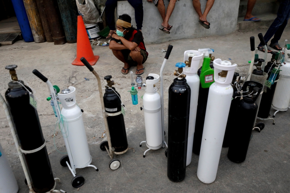 Firmansyah, a 52-year-old man, squats while queuing to refill oxygen tanks for his neighbor who has breathing problems as Indonesia experiences an oxygen supply shortage amid a surge of coronavirus disease (COVID-19) cases, at a filling station in Jakarta