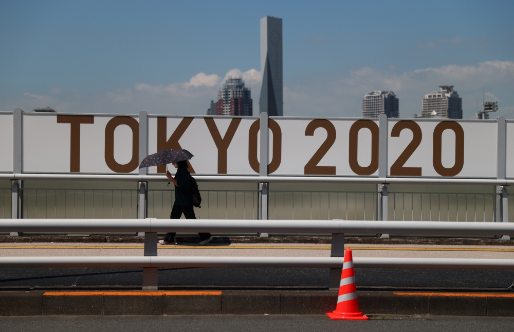 July 19, 2021 A woman shelters from the sun under an umbrella as she walks past Olympics signage REUTERS/Thomas Peter