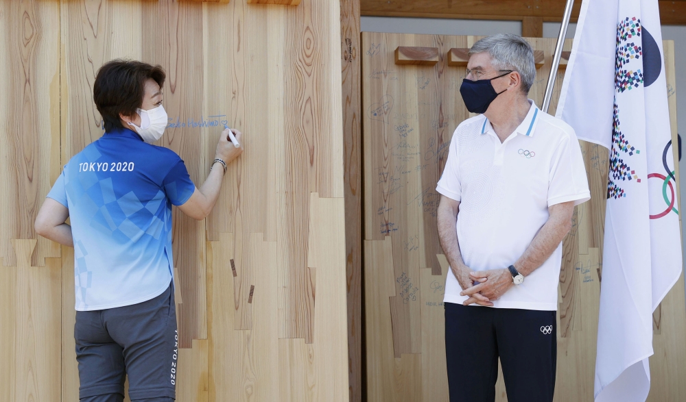 Tokyo 2020 President Seiko Hashimoto signs her autograph on a mural set up to wish for a truce in warring areas of the world during the Olympic Games while IOC President Thomas Bach looks on, at the athletes' village in Tokyo, Japan July 19, 2021. Kyodo/v