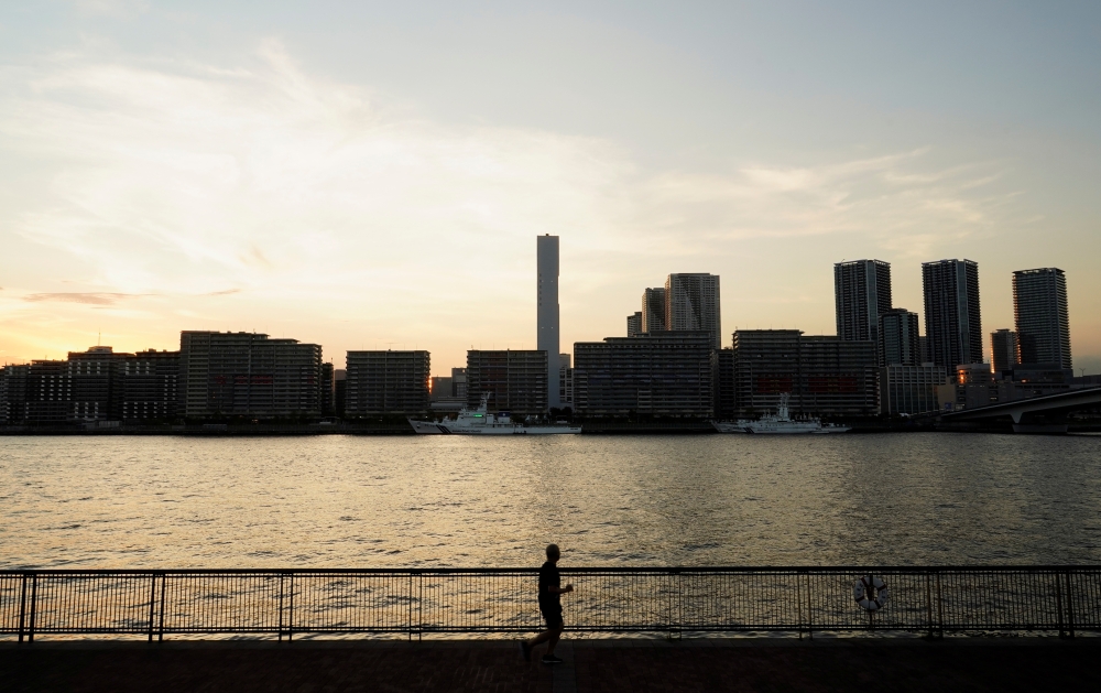 A person jogs as the 2020 Tokyo Olympic Games Athletes' Village is seen in the background, in Tokyo, Japan, July 19, 2021. REUTERS/Naoki Ogura