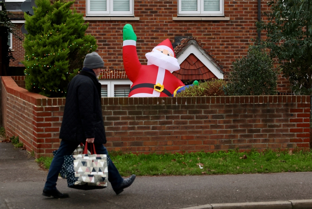 A man carrying shopping bags walks past a partially deflated blow-up Santa Claus amid the coronavirus disease (COVID-19) pandemic, in London, Britain December 20, 2021. REUTERS/Kevin Coombs