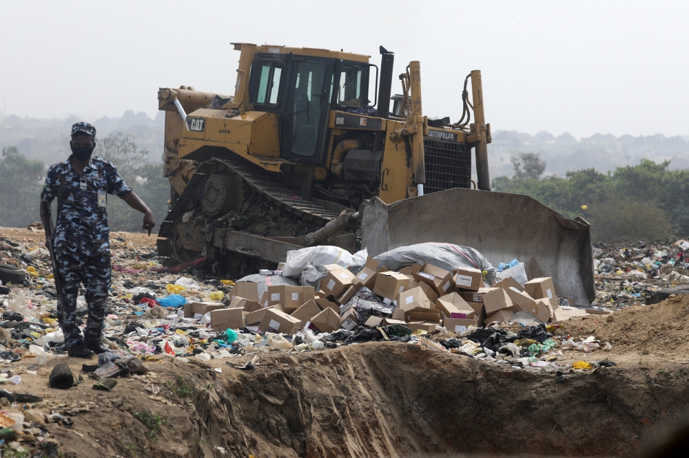 A police officer stands next to boxes of expired AstraZeneca coronavirus disease (COVID-19) vaccines at the Gosa dump site in Abuja, Nigeria December 22, 2021. REUTERS/Afolabi Sotunde
