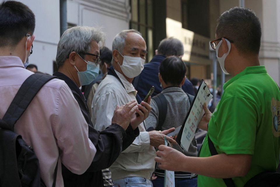 A staff member holds a QR code for the “LeaveHomeSafe” COVID-19 contact-tracing app to people lining up outside a community vaccination centre providing Sinovac Biotech's CoronaVac COVID-19 vaccine in Hong Kong, China December 2, 2021. REUTERS/Lam Yik

