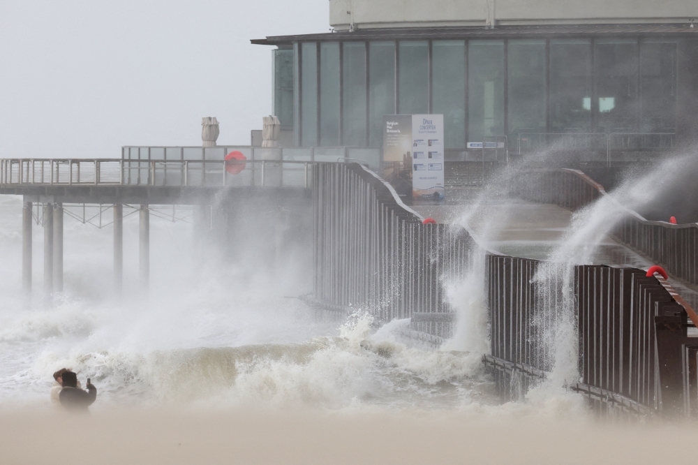 People take pictures as waves break on the beach in the wake of Storm Eunice in Blankenberge, Belgium, February 18, 2022. REUTERS/Yves Herman