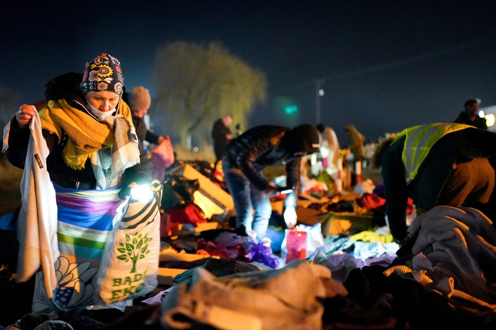 A woman searches through donated clothes for useful items after she and her children fled the Russian invasion in Ukraine and crossed the border in Medyka, Poland February 27, 2022. Reuters/Bryan Woolston