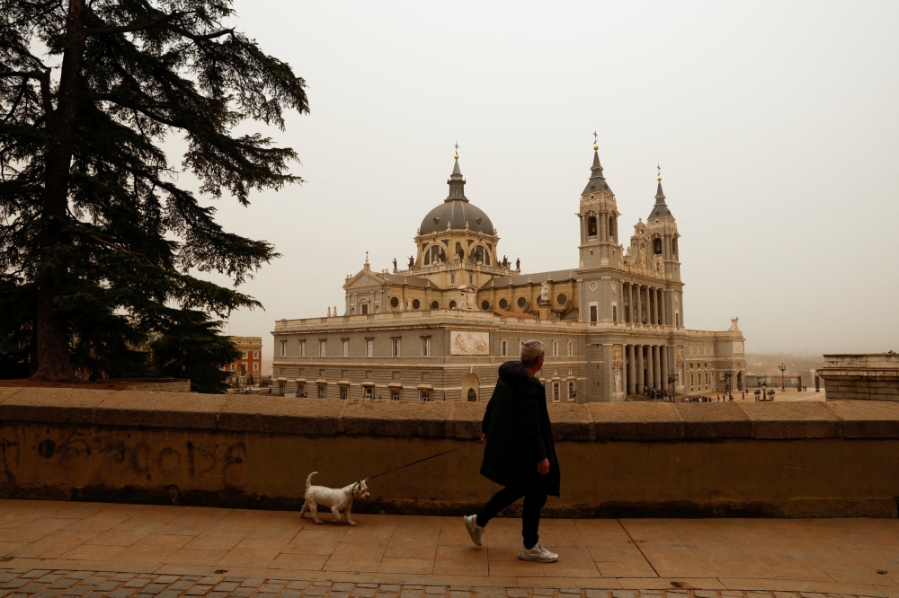 A man walks his dog near Almudena Cathedral, as storm Celia blew sand from the Sahara desert over Madrid, Spain, March 15, 2022. REUTERS/Susana Vera