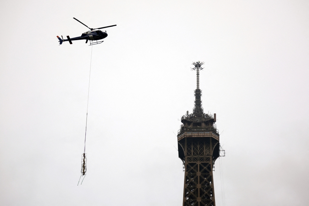 A helicopter flies next to the Eiffel Tower to install a new telecom transmission TDF (TeleDiffusion de France) antenna on its top, in Paris, France, March 15, 2022. REUTERS/Sarah Meyssonnier